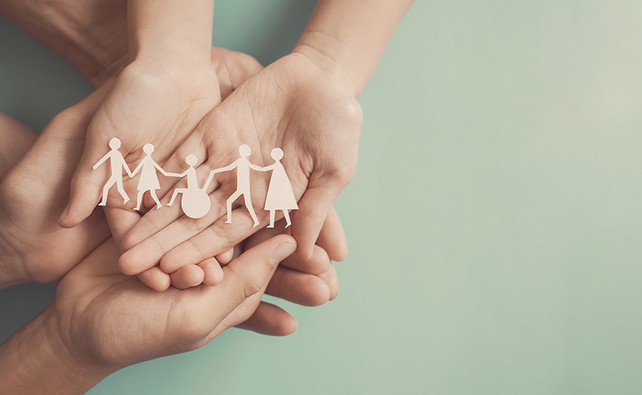 Hands holding paper cutout of differently abled people