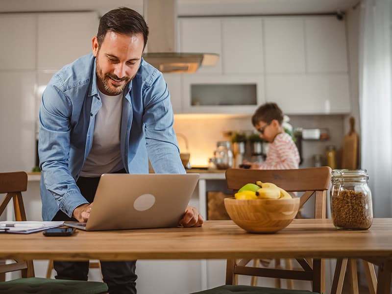 Father watching a recording of a recent school board meeting in the kitchen while his son plays on a phone.