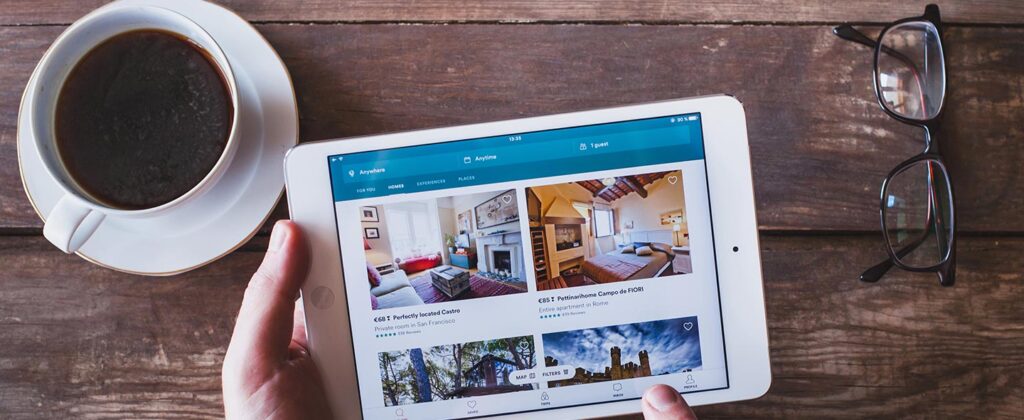 Person sitting at a table drinking coffee and browsing short-term rentals on their tablet