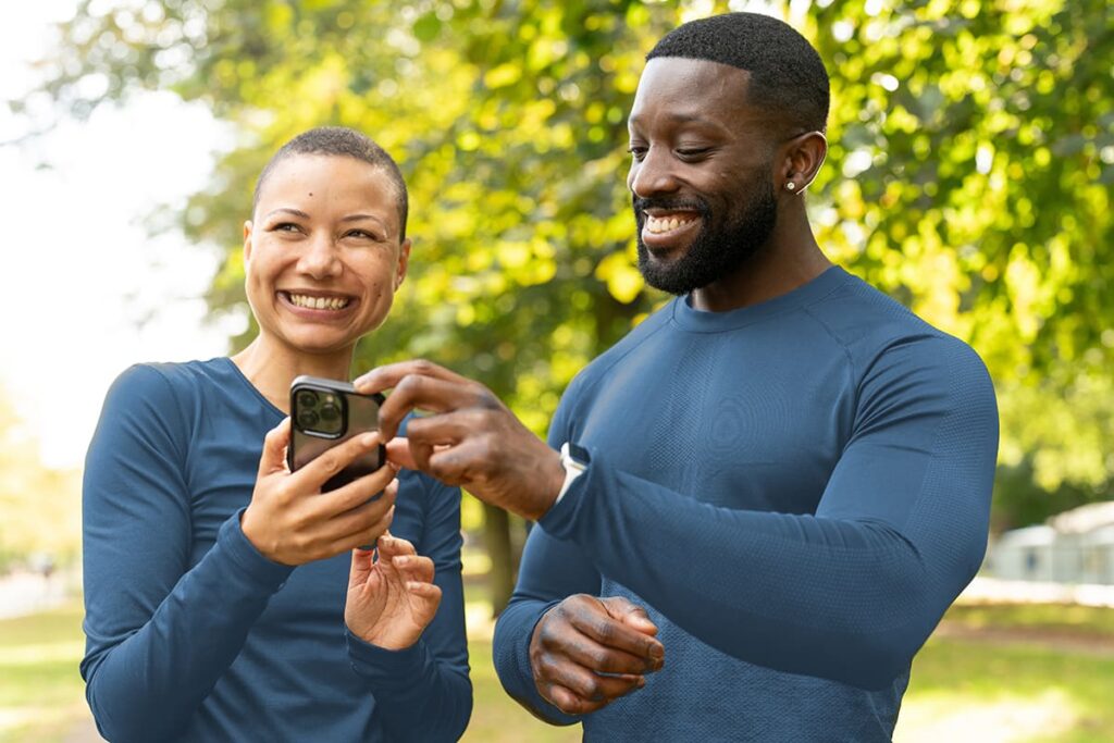 African American man and woman in a park smiling while looking at their mobile device